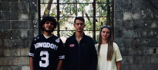 Three people standing in front of a stone wall with large windows.