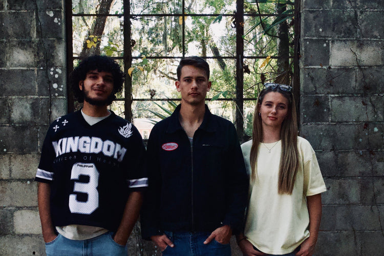 Three people standing in front of a stone wall with large windows.